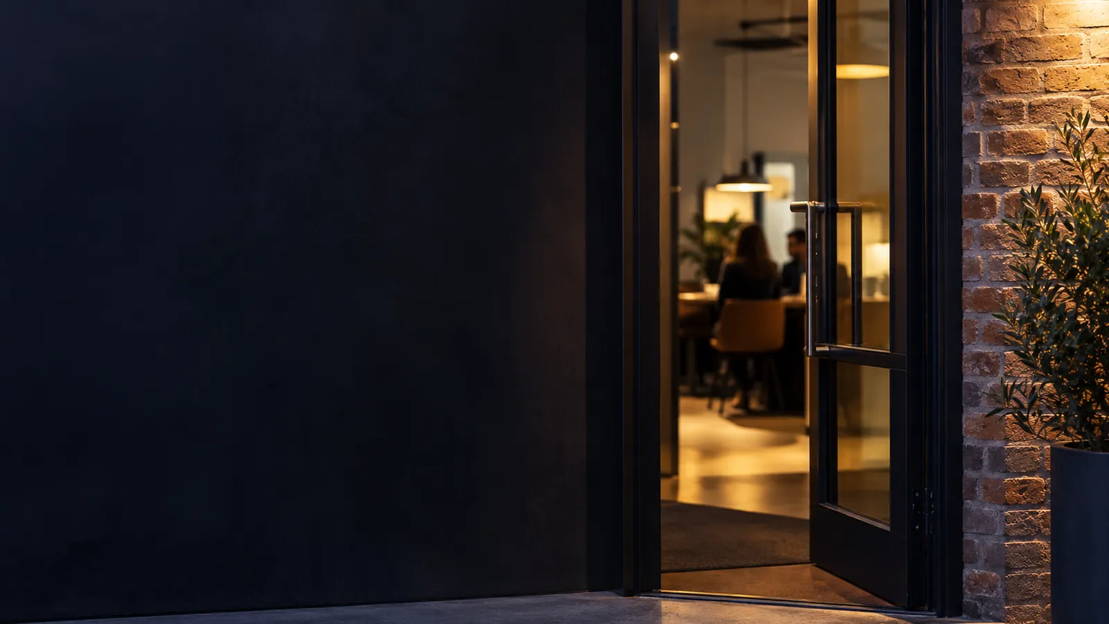 Porte vitrée entrouverte d'un bureau aux murs de brique, lumière chaude venant de l'intérieur