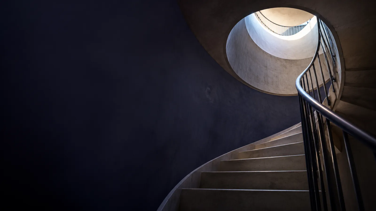 Escalier en colimaçon minimaliste vu d'en bas, montant vers une ouverture lumineuse, symbole de progression