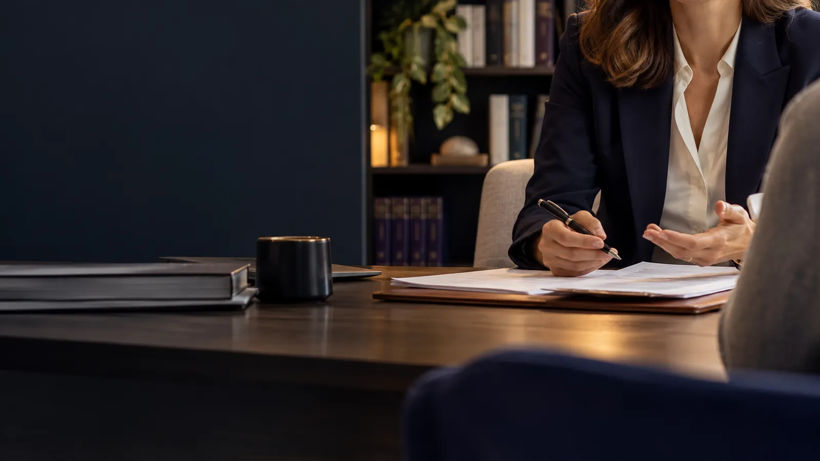 Professionnelle libérale prenant des notes face à un interlocuteur de dos, dans un cabinet sobre aux étagères de livres